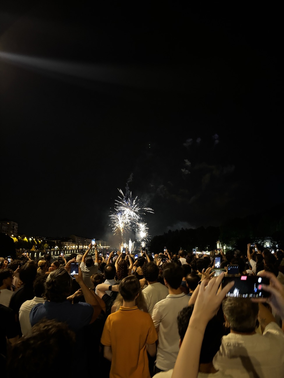 La folla stipata lungo il Po durante i fuochi di San Giovanni, a Torino, con i telefoni alzati verso lo spettacolo.